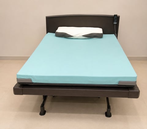 Modern adjustable bed frame with light blue mattress, dark headboard, and two black pillows