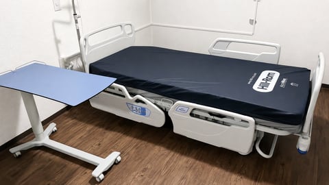 Medical examination room with adjustable hospital bed and blue patient table on wooden floor