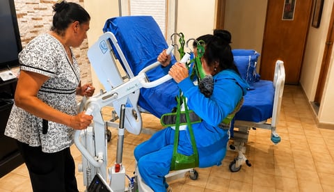 Healthcare worker in blue scrubs operating a medical device while patient in patterned shirt receives treatment indoors